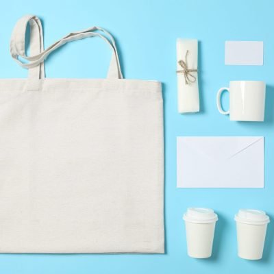 Flat lay composition with cotton bag, paper cups and office supplies on blue background
